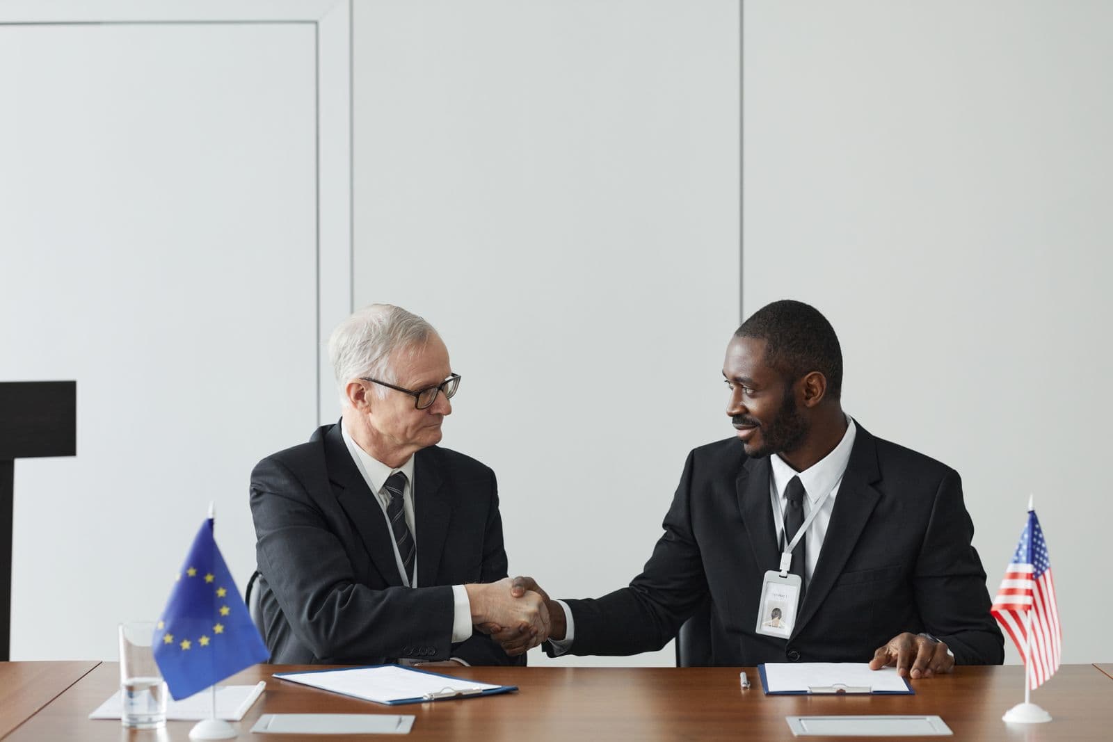 Poignée de main entre deux dirigeants, drapeaux européen et américain sur la table