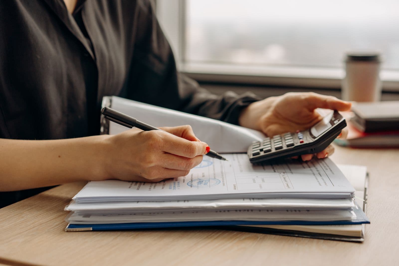Personne utilisant une calculatrice sur une pile de documents financiers